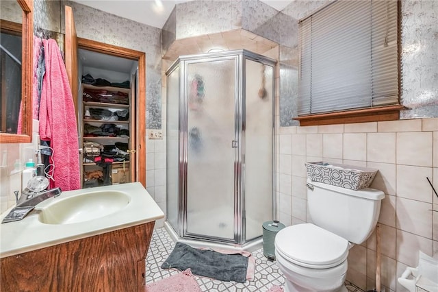 bathroom with tile patterned floors, vanity, a shower with door, tile walls, and toilet