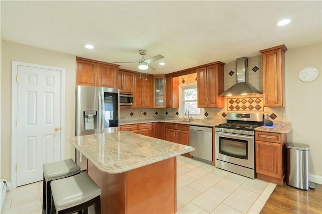 kitchen featuring sink, wall chimney exhaust hood, ceiling fan, light stone countertops, and stainless steel appliances