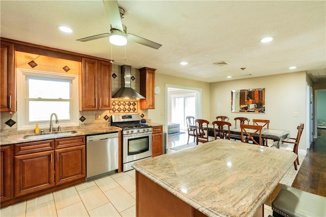 kitchen featuring sink, wall chimney exhaust hood, stainless steel appliances, light stone counters, and decorative backsplash