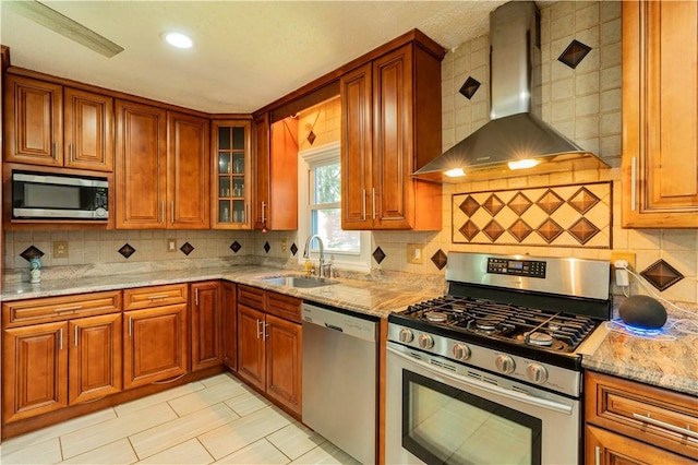 kitchen featuring light stone countertops, sink, wall chimney range hood, decorative backsplash, and appliances with stainless steel finishes