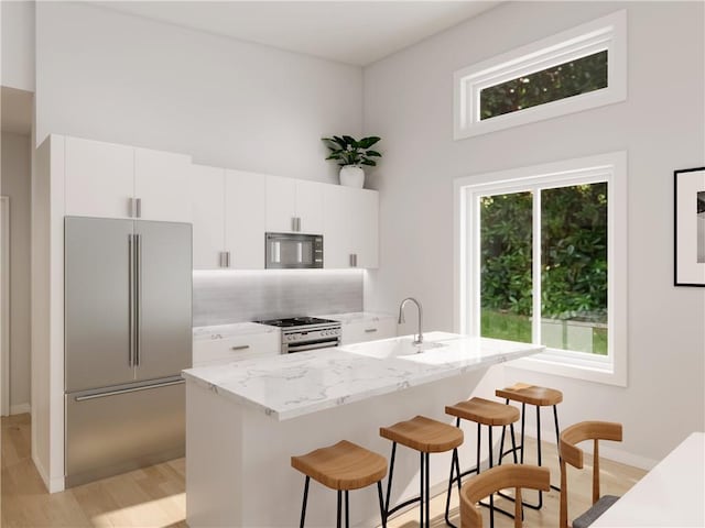 kitchen featuring appliances with stainless steel finishes, sink, light hardwood / wood-style flooring, white cabinetry, and a breakfast bar area