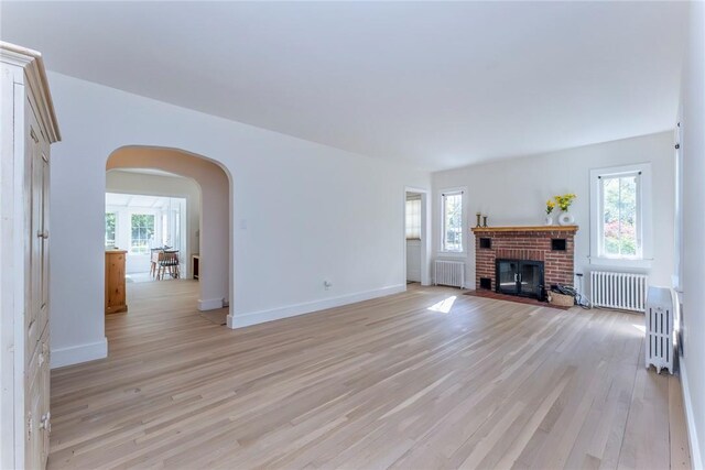 unfurnished living room featuring radiator, light hardwood / wood-style floors, and a brick fireplace