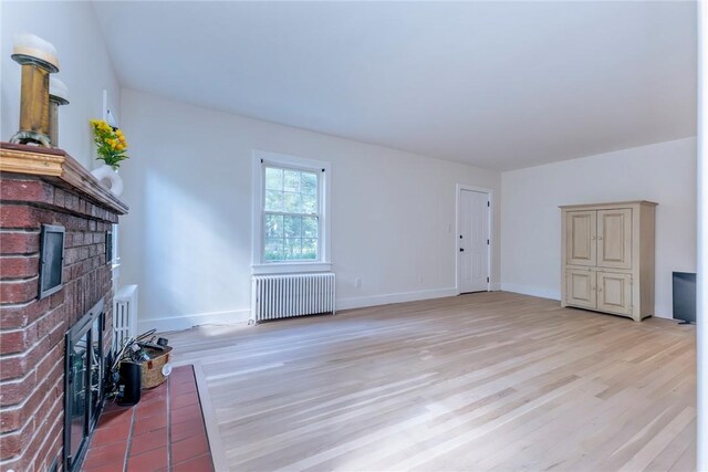 unfurnished living room with light wood-type flooring, radiator heating unit, and a brick fireplace