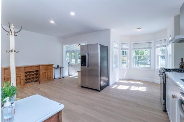 kitchen with white cabinets, stainless steel appliances, wall chimney range hood, and light wood-type flooring