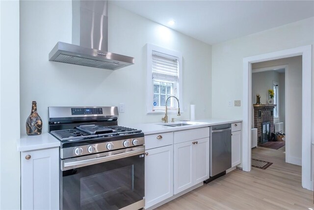 kitchen with appliances with stainless steel finishes, wall chimney exhaust hood, sink, light hardwood / wood-style flooring, and white cabinetry