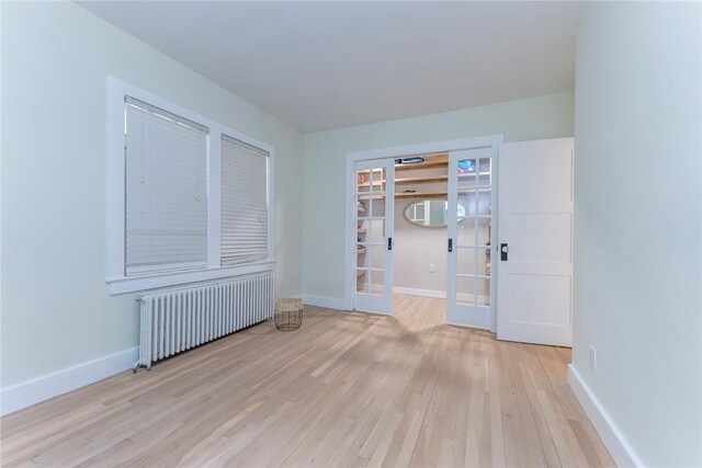 unfurnished room featuring radiator heating unit, light hardwood / wood-style flooring, and french doors