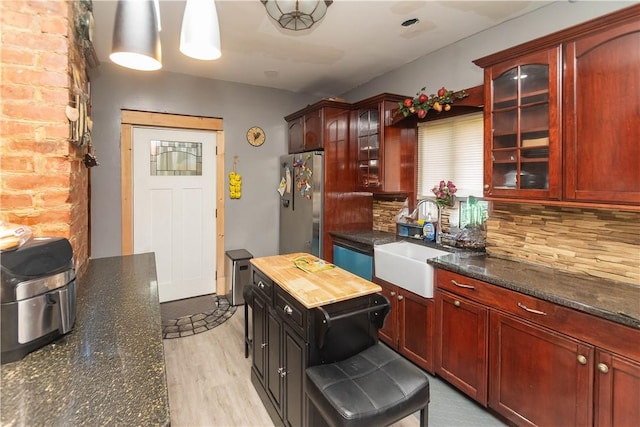 kitchen with sink, hanging light fixtures, dark stone countertops, stainless steel fridge, and light wood-type flooring