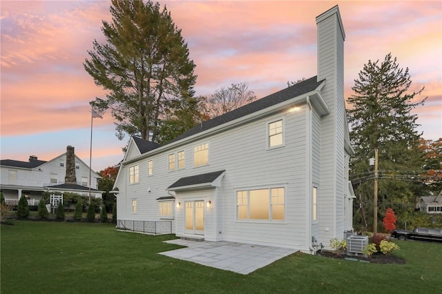 back house at dusk featuring a lawn, a patio, and central AC unit