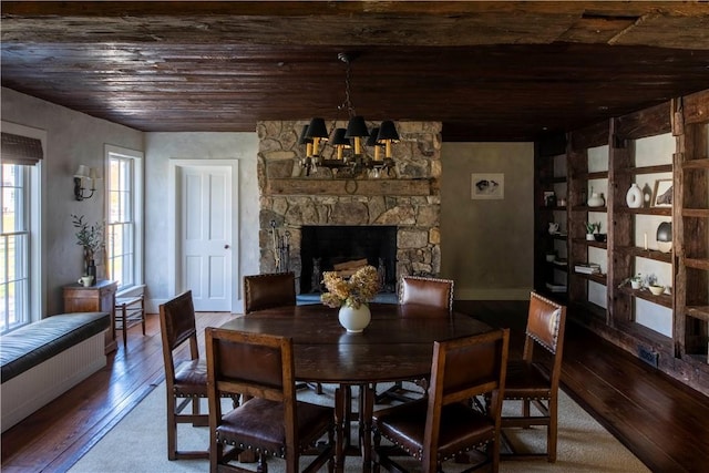 dining space with wooden ceiling, hardwood / wood-style flooring, an inviting chandelier, and a stone fireplace