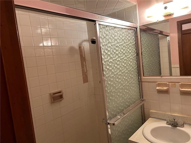 bathroom with a shower with shower door, sink, and tile walls