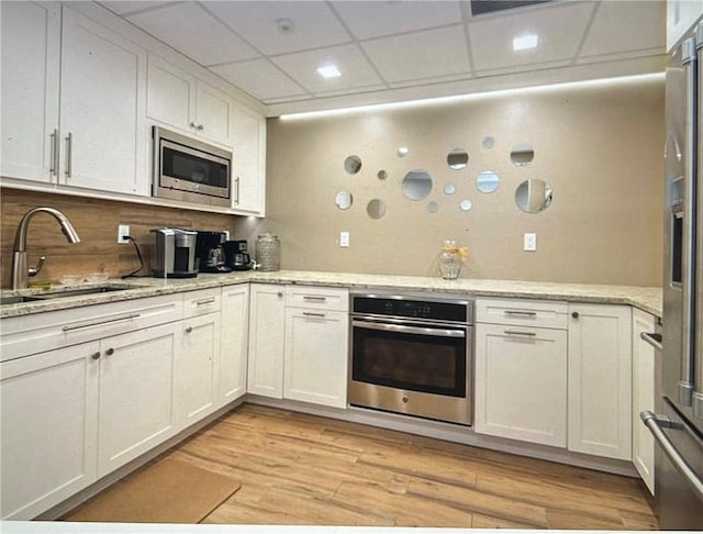 kitchen with appliances with stainless steel finishes, white cabinetry, sink, decorative backsplash, and a drop ceiling