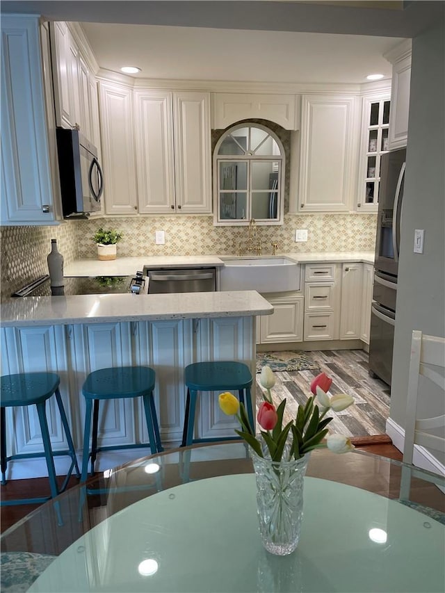 kitchen with white cabinetry, dishwasher, sink, a kitchen bar, and kitchen peninsula