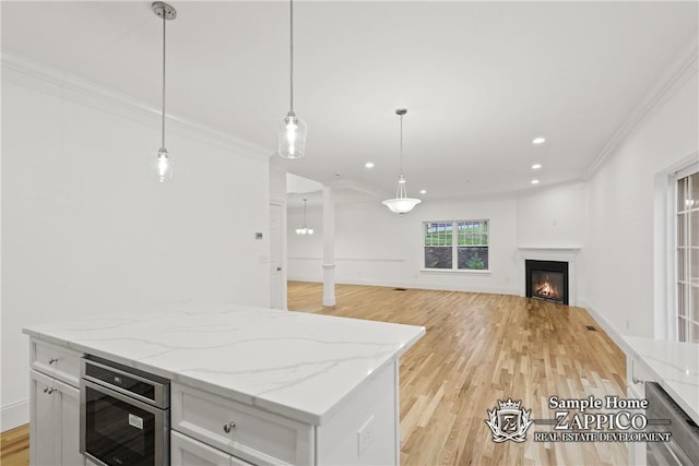 kitchen with white cabinets, crown molding, hanging light fixtures, light wood-type flooring, and light stone counters