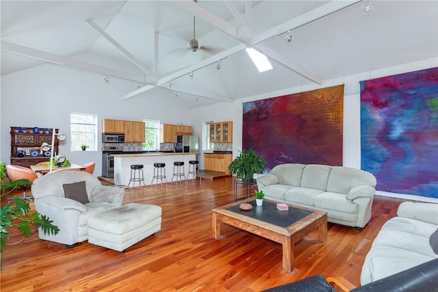 living room with track lighting, a skylight, ceiling fan, light wood-type flooring, and beamed ceiling