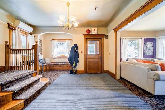 entrance foyer with an AC wall unit, dark colored carpet, a healthy amount of sunlight, and an inviting chandelier