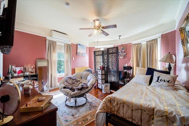 bedroom with a wall mounted AC, wood-type flooring, ceiling fan, and radiator