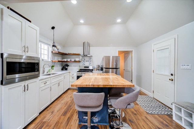 kitchen with sink, range hood, vaulted ceiling, white cabinets, and appliances with stainless steel finishes