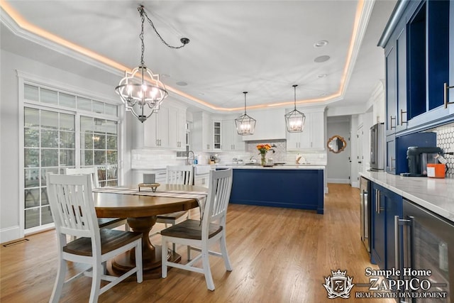 dining space featuring a tray ceiling, crown molding, beverage cooler, and light wood-type flooring