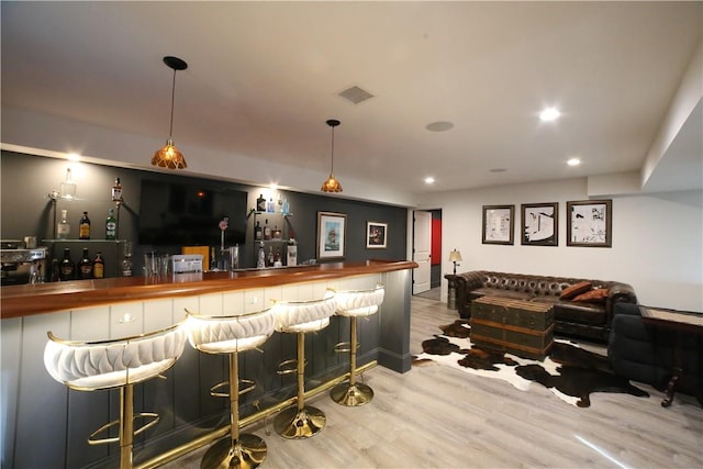 bar featuring butcher block counters, light hardwood / wood-style floors, and decorative light fixtures