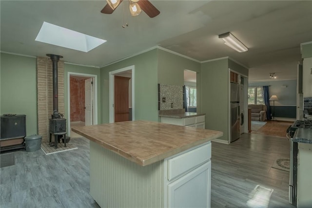 kitchen featuring a wood stove, white cabinetry, light hardwood / wood-style flooring, a kitchen island, and ornamental molding