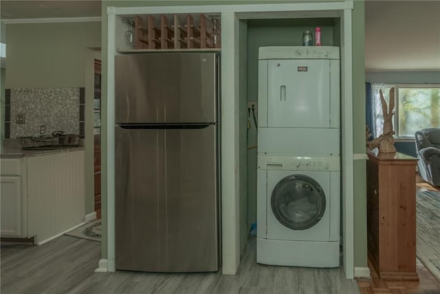 laundry room featuring stacked washer / drying machine, light hardwood / wood-style floors, and crown molding