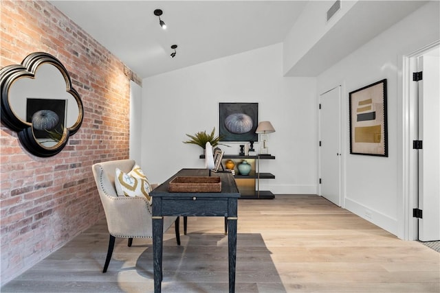 office area featuring light wood-type flooring, lofted ceiling, and brick wall