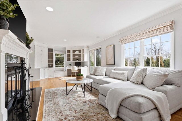 living room with light wood-style floors, recessed lighting, crown molding, and a high end fireplace