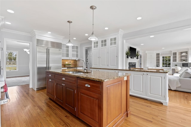 kitchen featuring a center island with sink, glass insert cabinets, open floor plan, built in refrigerator, and a sink