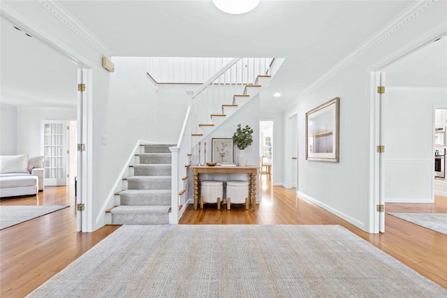 stairs with ornamental molding, wood finished floors, and baseboards