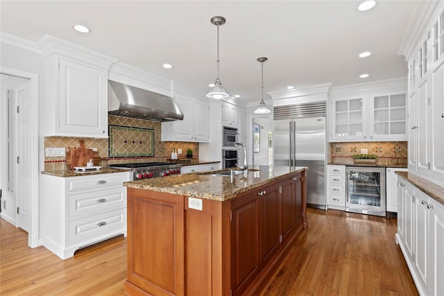 kitchen featuring dark stone counters, wine cooler, glass insert cabinets, stainless steel appliances, and wall chimney range hood