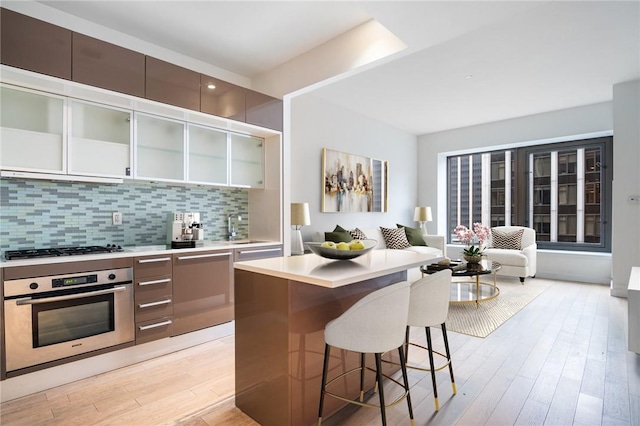 kitchen with decorative backsplash, sink, appliances with stainless steel finishes, and light hardwood / wood-style flooring