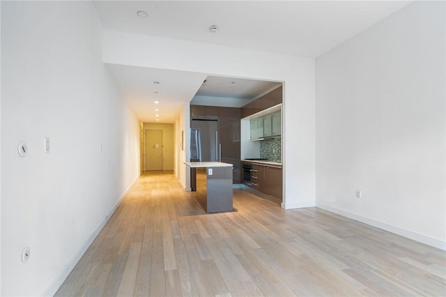 kitchen with a center island, decorative backsplash, light wood-type flooring, appliances with stainless steel finishes, and a kitchen bar