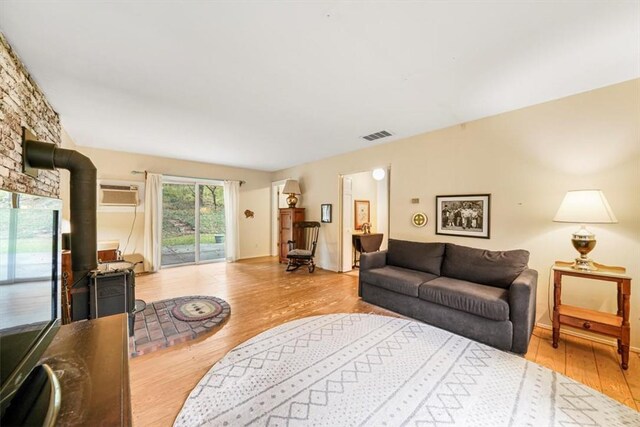 living room featuring an AC wall unit, a wood stove, and light hardwood / wood-style flooring