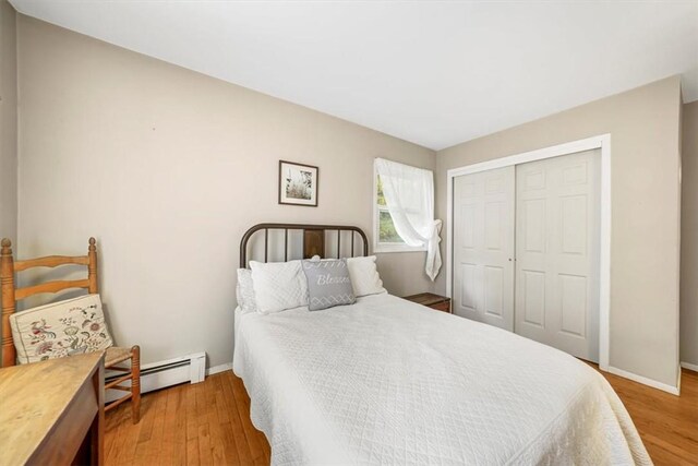 bedroom with a baseboard heating unit, wood-type flooring, and a closet