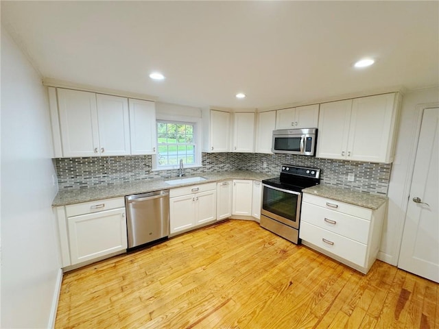 kitchen with light wood-type flooring, light stone counters, stainless steel appliances, sink, and white cabinets