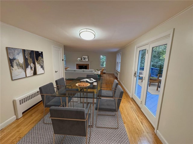 dining area with a fireplace, light wood-type flooring, radiator, and crown molding