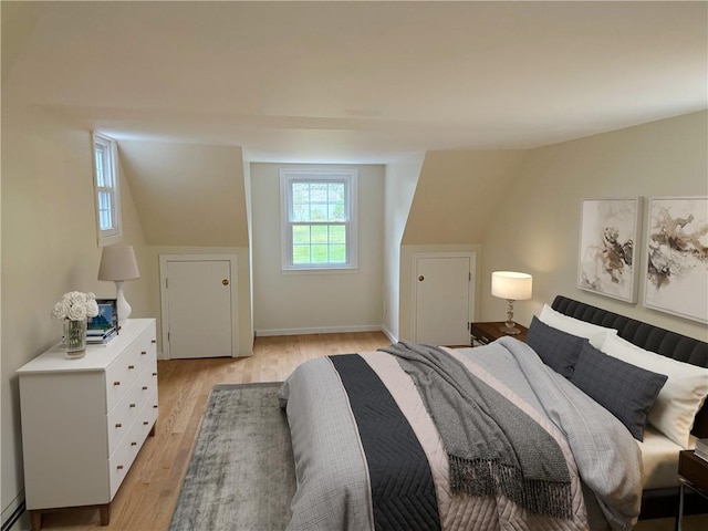 bedroom featuring a baseboard heating unit, light hardwood / wood-style flooring, and lofted ceiling