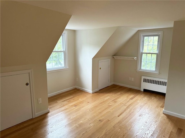 additional living space with lofted ceiling, radiator heating unit, plenty of natural light, and light hardwood / wood-style flooring