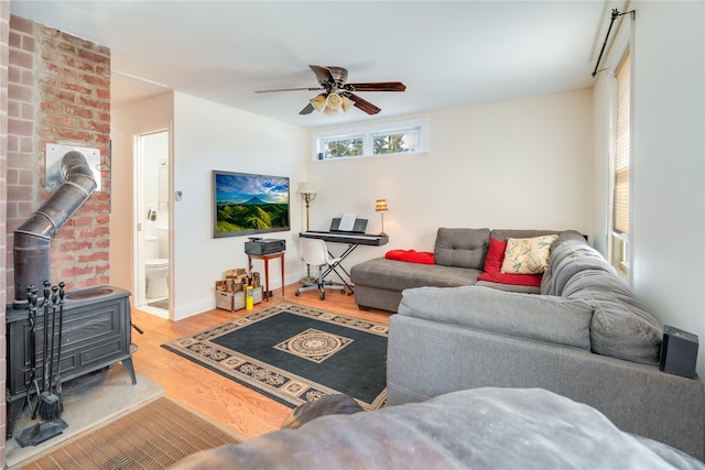 living area featuring baseboards, a ceiling fan, wood finished floors, and a wood stove