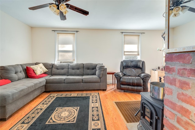 living room with a wealth of natural light, wood finished floors, a wood stove, and ceiling fan