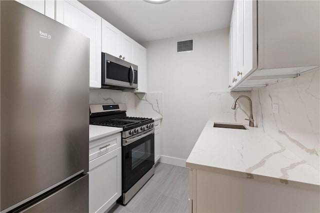 kitchen with white cabinets, sink, light stone countertops, appliances with stainless steel finishes, and tasteful backsplash