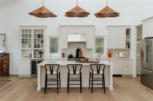 kitchen with appliances with stainless steel finishes, pendant lighting, range hood, wine cooler, and an island with sink