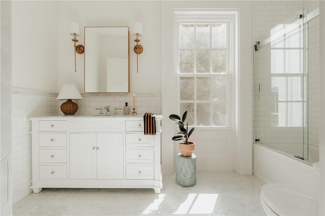 full bathroom featuring vanity, shower / bath combination with glass door, tile patterned floors, toilet, and tile walls