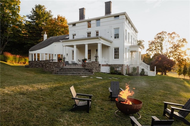 rear view of house with a fire pit, covered porch, and a yard