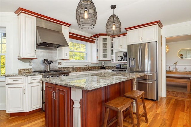 kitchen with light wood-type flooring, ornamental molding, wall chimney exhaust hood, stainless steel appliances, and a center island