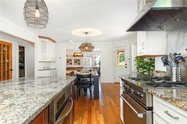 kitchen featuring white cabinets, wall chimney exhaust hood, hanging light fixtures, and stainless steel stove