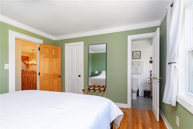 bedroom with ensuite bathroom, light hardwood / wood-style flooring, crown molding, and a notable chandelier