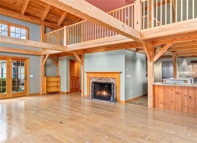 unfurnished living room with beamed ceiling, wood ceiling, a high ceiling, and light wood-type flooring