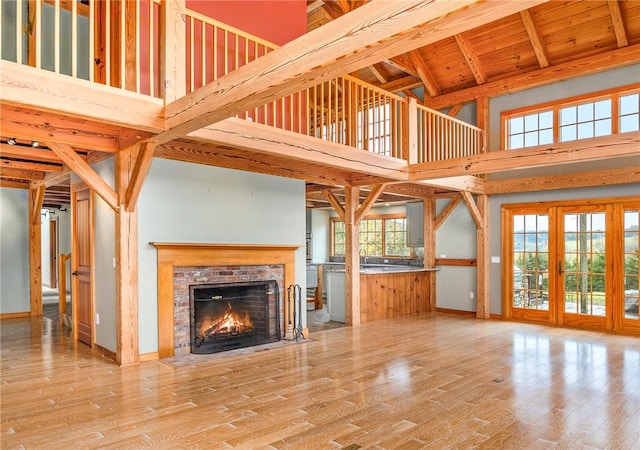 unfurnished living room featuring a brick fireplace, light wood-type flooring, high vaulted ceiling, and plenty of natural light