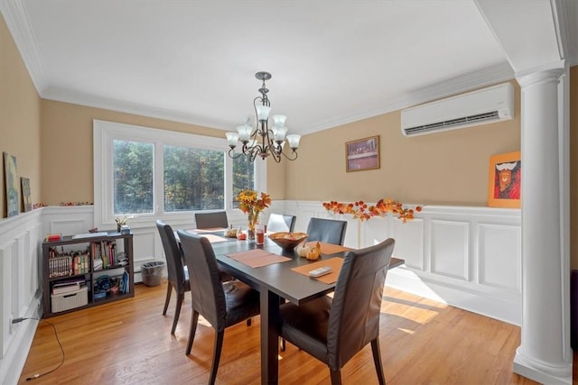 dining space featuring a notable chandelier, an AC wall unit, decorative columns, light hardwood / wood-style floors, and ornamental molding